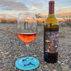 A blue Wine Glass Slipper sitting on rocks with bottle of red wine beside in stunning background with sunset.