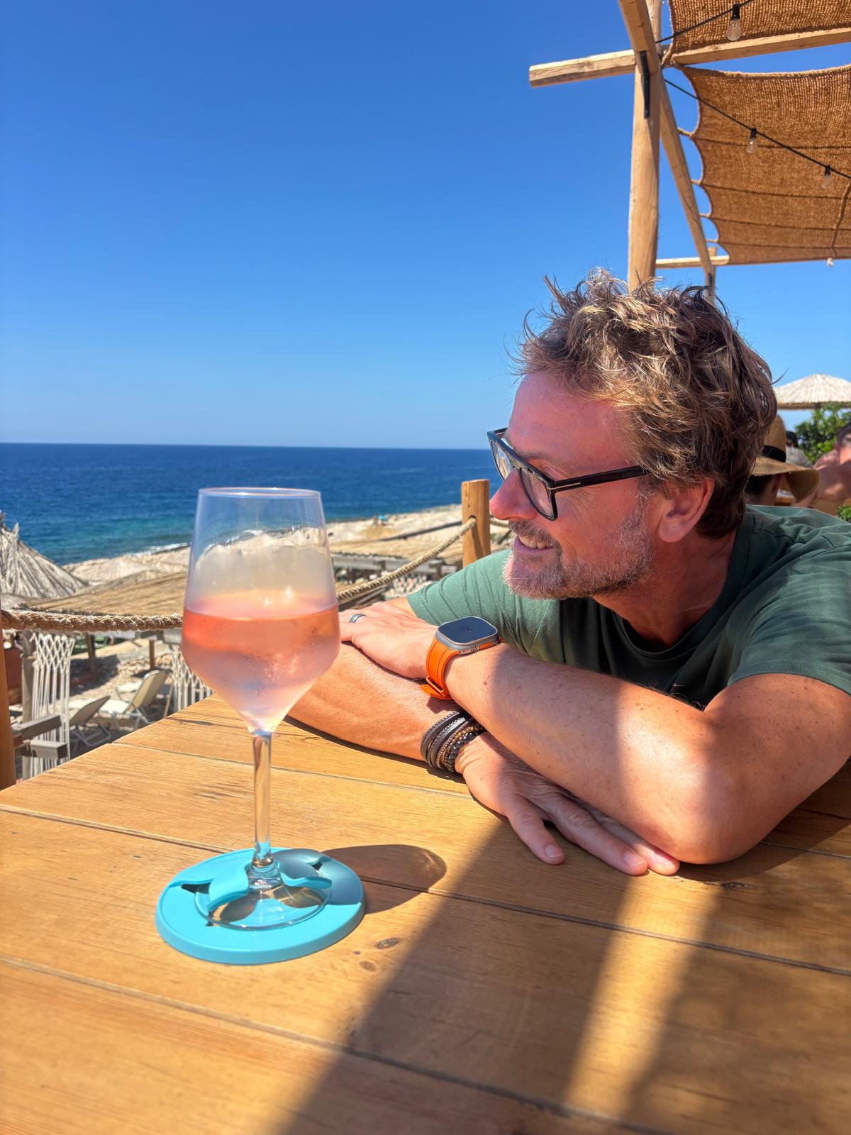 Man sitting at a table by the ocean with a glass of Rosé wine.in a stemmed glass The Glass Slipper coaster