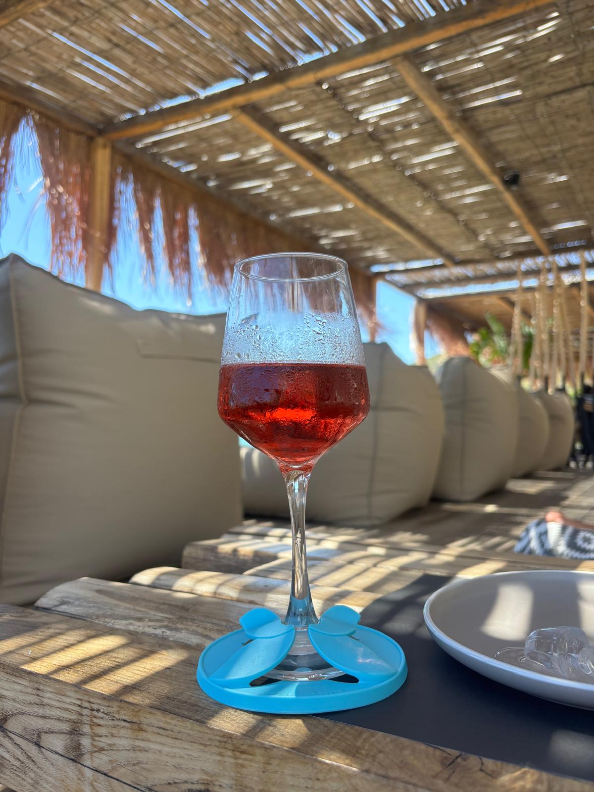 Wine glass with Rosé wine with The Glass Slipper coaster on a table under a thatched roof at the beach